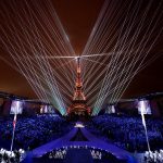View of the Paris Olympics 2024 Opening Ceremony, showcasing a vibrant blend of lights, art, and culture with iconic Parisian landmarks illuminated against the night sky. Athletes and performers take center stage, celebrating global unity and the rich cultural heritage of France.