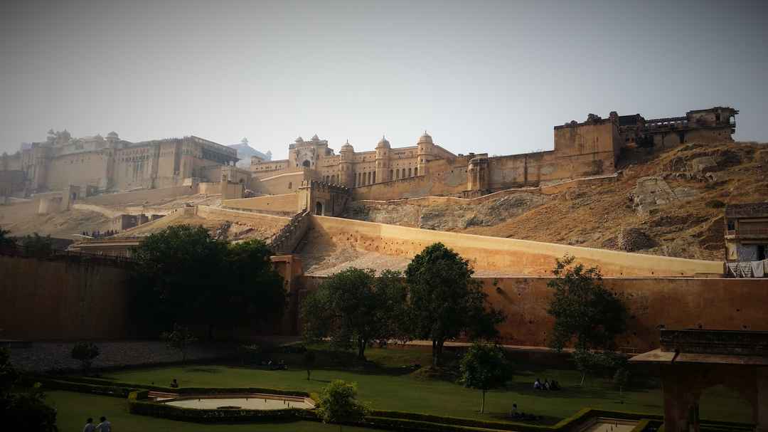 A majestic view of Jaipur, Rajasthan, during winter, highlighting its iconic pink sandstone architecture, grand palaces, and historic forts. The scene features the Amber Fort perched on a hill, lush winter gardens, and bustling markets adorned with colorful textiles and traditional crafts, all set against a clear, crisp sky