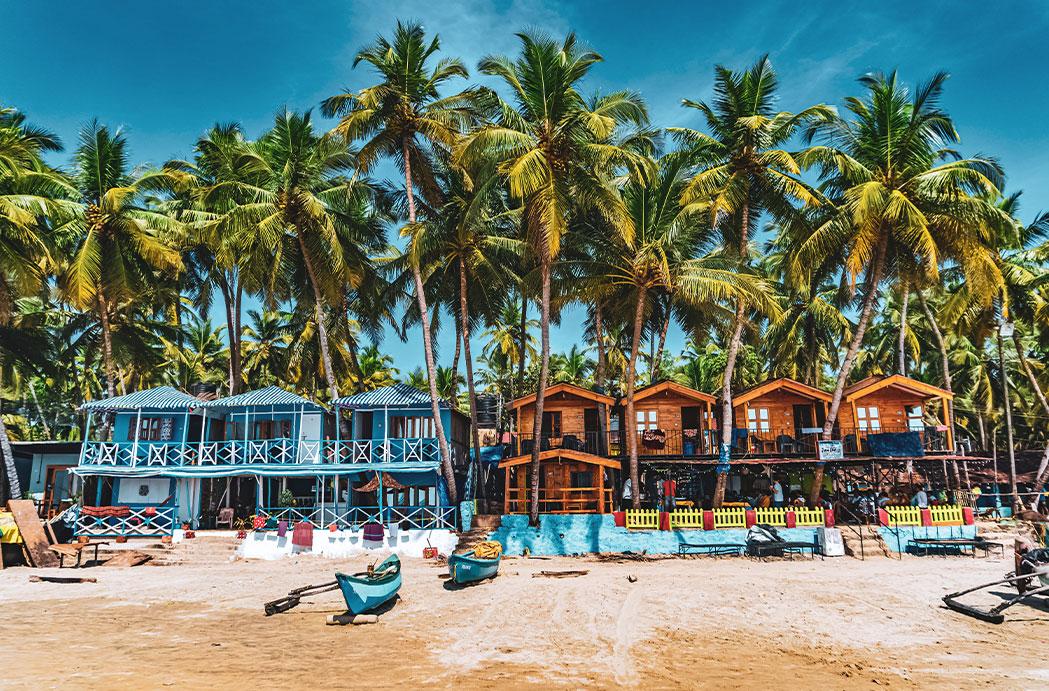 A vibrant coastal scene of Goa during winter, featuring golden sandy beaches lined with swaying palm trees, lively beach shacks, and colorful umbrellas. Tourists enjoy water sports, bonfires, and music under a vivid sunset, capturing the festive and energetic spirit of the season.